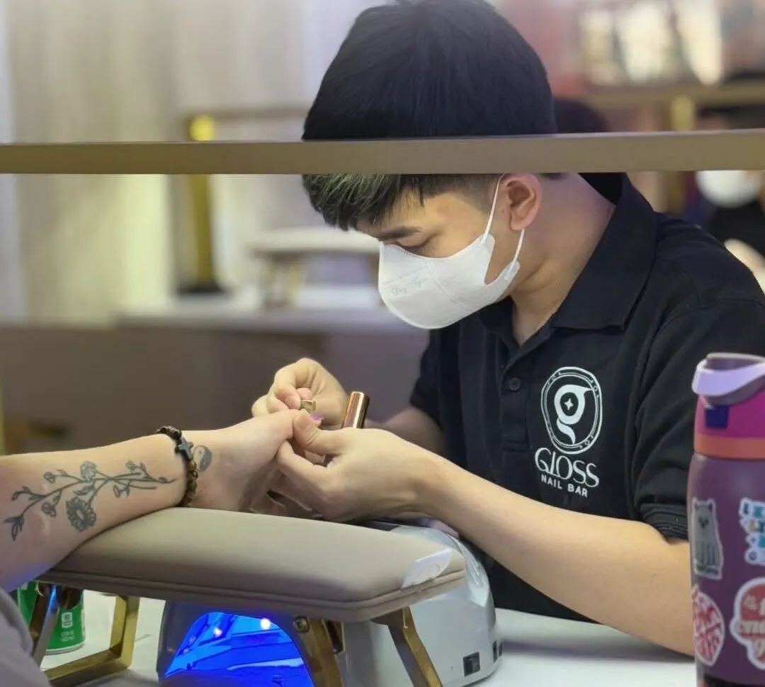 A Gloss Niles nail technician at work, hand-finishing a guest's manicure under the UV lamp
