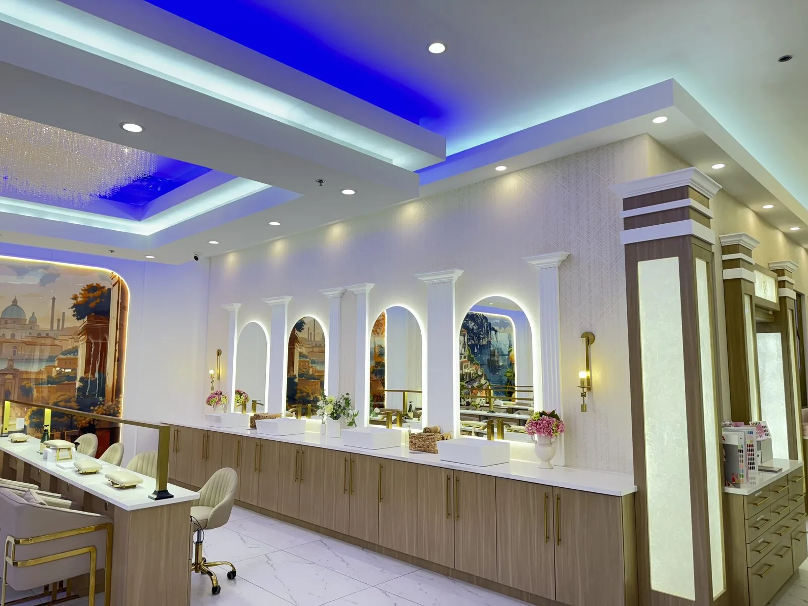 White-columned vanity wall with arched Mediterranean murals, gold sconces and fresh florals