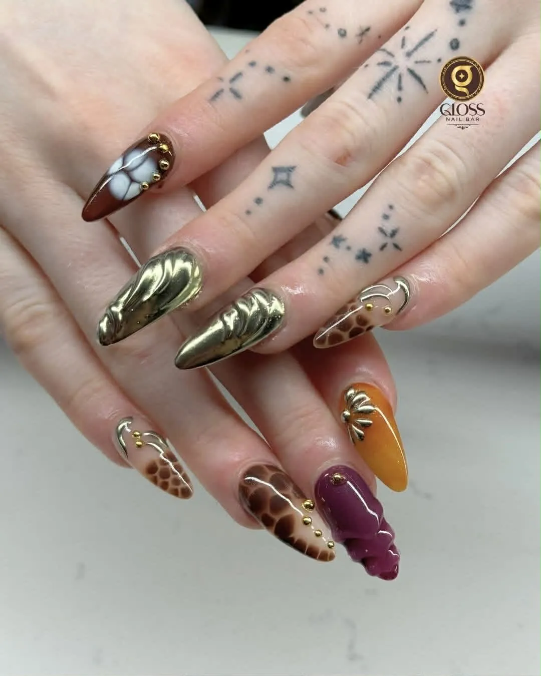 Gold chrome almond nails with giraffe and snakeskin prints and a 3D purple charm